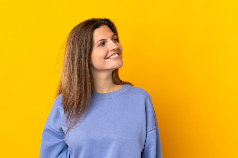 eine Frau in einem blauen Pullover, der vor einem gelben Hintergrund steht