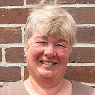 Die stolze Weiterbildungsteilnehmerin Astrid Estel steht, die Hände auf die Hüften gestützt, vor einer geziegelten Hauswand.