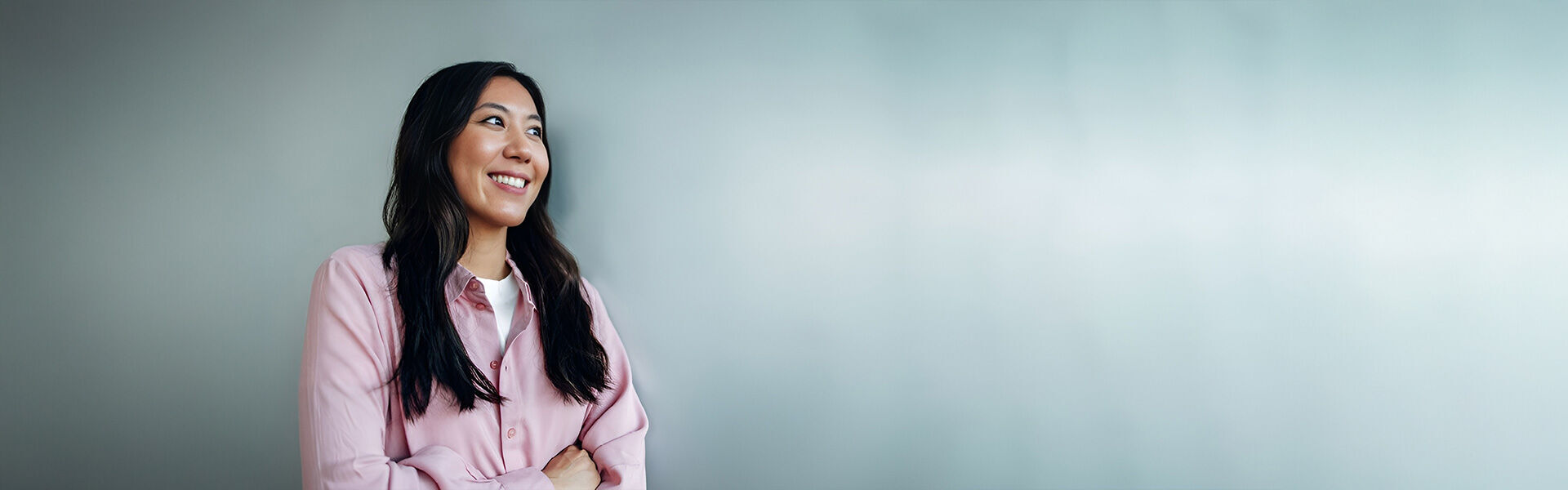 eine Frau in einer rosa Bluse verschränkt die Arme und lächelt